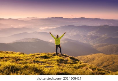 Sporty man standing on the mountain peak with raised up arms against mountain valley in fog at sunset in autumn. Happy young man, rocks, forest and blue sky in fall. Traveler hiking in mountains - Powered by Shutterstock