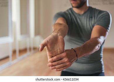 Sporty man stretching arm before gym workout. Fitness strong male athlete standing indoor warming up.