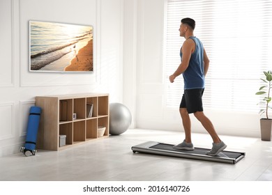 Sporty Man Training On Walking Treadmill And Watching TV At Home