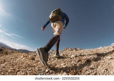 Sporty man walk with backpack uphill in mountains. Close up photo from bottom view