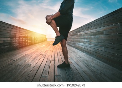 Sporty man warming up and stretching legs before workout outdoors at sunset or sunrise. Stretching gluteus maximus muscle. Athletic man doing fitness stretching exercises. Sport and healthy lifestyle