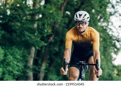 Sporty man wearing active wear and helmet riding a black bike in nature. Concept of people, workout and favorite hobby. Copy space. Looking into the camera.