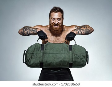 Sporty man working out, holds heavy sandbag. Photo of man with naked torso on grey background. Strength and motivation