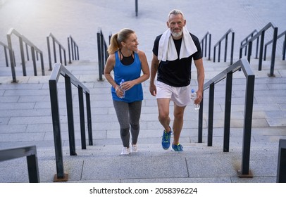 Sporty Mature Couple, Man And Woman In Sportswear Looking Pleased, Walking Up The Stairs After Training Together Outdoors