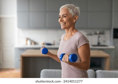 Sporty mature lady lifts blue dumbbells maintaining fitness in modern home interior, leading active sporty lifestyle and keeping fit in retirement, enjoying domestic exercises - Powered by Shutterstock