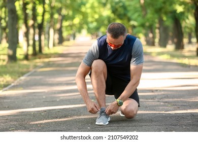 Sporty Mature Man Tying Shoe Laces In Park