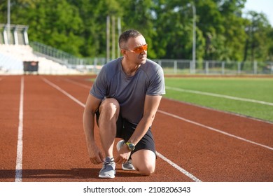 Sporty Mature Man Tying Shoe Laces At Stadium