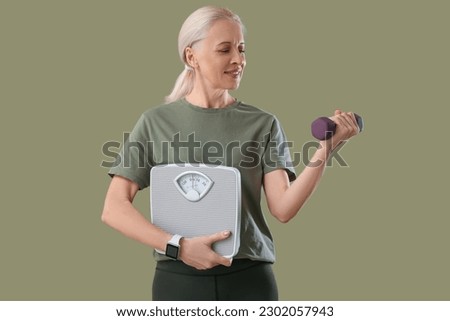 Sporty mature woman with scales and dumbbell on green background