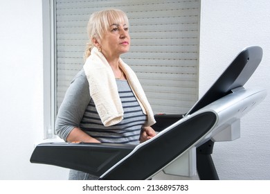 Sporty Mature Woman With Towel Around Her Neck Walking On Treadmill At Home