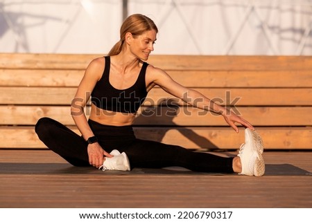Sporty Middle Aged Female Stretching Leg Muscles After Jogging Outdoors, Beautiful Athletic Woman In Activewear Sitting On Wooden Pier, Exercising And Enjoying Outside Workout, Free Space