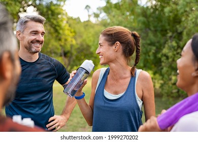 Sporty middle aged woman drinking water from bottle after fitness exercise. Latin mature woman drinking water for refreshment after workout in park while talking and smiling with a group of friends. - Powered by Shutterstock