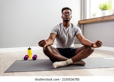 Sporty mindful man with tattoo meditating alone at home, peaceful calm hipster fit guy practicing yoga in lotus pose indoors holding hands in mudra, freedom and calmness concept, close up view