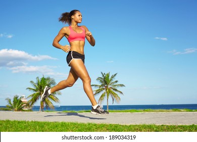 Sporty mixed race woman jogging. Color image, copy space, african american ethnicity female running with green grass and blue sky. - Powered by Shutterstock