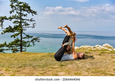 Sporty Mom And Her Adorable Kid Doying Dly Yoga On A Grass Of Island Olkhon With Baikal Lake On Background