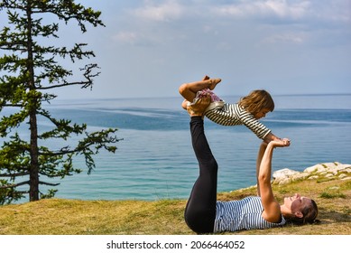 Sporty Mom And Her Adorable Kid Doying Dly Yoga On A Grass Of Island Olkhon With Baikal Lake On Background