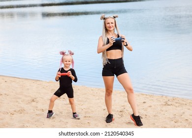 Sporty Mom And Her Daughter On The Beach With Dumbbells Exercising, Working Out. 