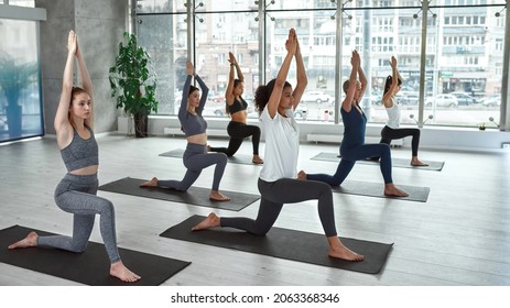 Sporty multiethnic women in warrior pose asana practice yoga at group training in gym. Active diverse females on mats meditate do sports workout training activity at class. Healthy lifestyle. Wide. - Powered by Shutterstock