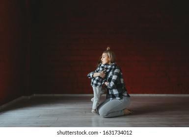 Sporty Mum And Cute Daughter, Relaxing After Training, Sitting And Embracing On Floor At Gym. Woman And Kid Wearing In Shirts And Jeanses Embrace Sitting On Floor.