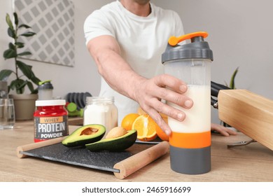 Sporty muscular man with protein shake on table in kitchen, closeup - Powered by Shutterstock