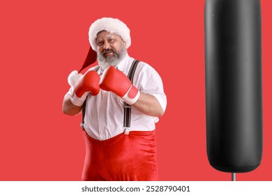 Sporty Santa Claus with boxing gloves punching bag on red background - Powered by Shutterstock