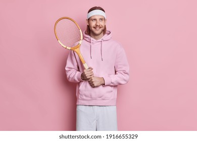 Sporty Satisfied Active Man With Mustache Holds Tennis Raquet Enjoys Playing Favorite Game During Spare Time Wears Headband And Hoodie Isolated Over Pink Background Prepares For Competition.