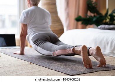 Sporty senior caucasian woman working out, doing urdhva mukha shvanasana or upward facing dog pose at home.