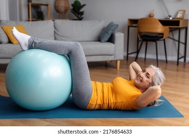 Sporty senior lady exercising her abs muscles with fitball on yoga mat at home, looking and smiling at camera, free space. Side view of fit aged woman leading active lifestyle - Powered by Shutterstock