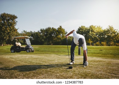 Sporty senior man placing a golf ball on a tee while standing on a golf course on a sunny day - Powered by Shutterstock