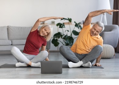 Sporty senior spouses training at home, smiling mature man and woman having workout together, using modern laptop, watching fitness class on Internet, home interior, copy space - Powered by Shutterstock