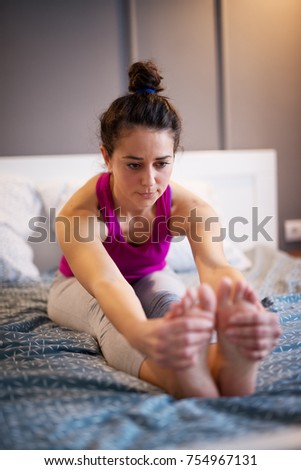 Sporty shape middle aged woman stretching yoga exercise while sitting forward on the bed while her hands are holding the feets. 