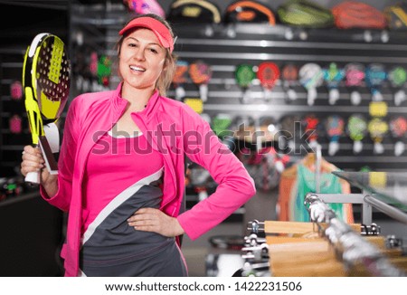 Sporty smiling woman in uniform is holding new racket for padel in the sports store