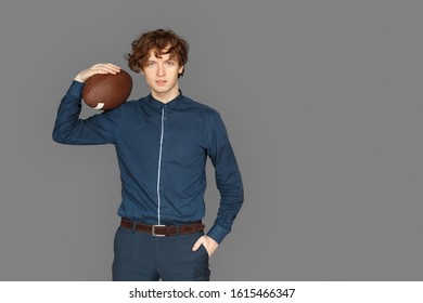 Sporty teenager boy standing isolated on grey background holding american football ball on shoulder hand in pocket posing to camera smiling confident - Powered by Shutterstock