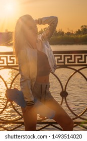 Sporty woman 30s with skateboard on waterfront in painterly sunset light, shot with sun flares backlit, warm sunset mood