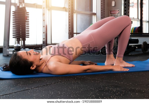 Sporty\
woman doing exercises doing Bridge position on blue mat. Healthy\
beautiful women doing glute Bridge exercise, pelvic lift abdominal\
exercise at home. Woman doing hip raise in\
gym.