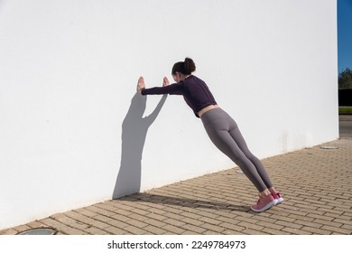 Sporty woman doing press ups against a white wall outside. - Powered by Shutterstock