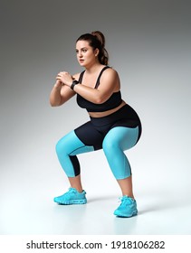 Sporty woman doing squats. Photo of model with curvy figure in fashionable sportswear on grey background. Sports motivation and healthy lifestyle