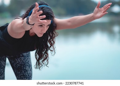 Sporty woman doing stretching exercises, strong and healthy, stretching arms, warming up for exercise in park, looking far away. Silhouette of young athlete prepares body for exercises. - Shutterstock ID 2230787741