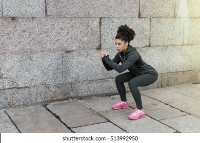 Sporty woman doing warm up squat, stretching near a wall