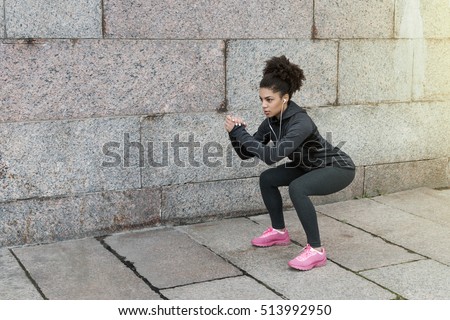 Sporty woman doing warm up squat, stretching near a wall
