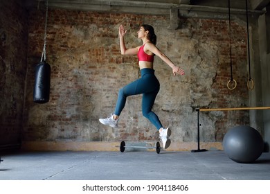 Sporty Woman During HIIT Workout. Dynamic Movement. Sportswoman Jumping High In The Process Of Training In The Gym