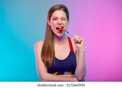 Sporty woman in fitness sportswear eating tomato on fork. Female fitness portrait isolated on neon multicolor background.