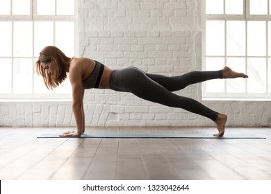 Sporty woman in grey sportswear, bra and leggings practicing yoga, doing Push ups or press ups exercise, phalankasana, variation of Plank pose, beautiful girl working out at home or in yoga studio