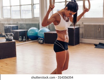 Sporty woman holding gymnast rings looking down. Young female athlete at gym with rings.