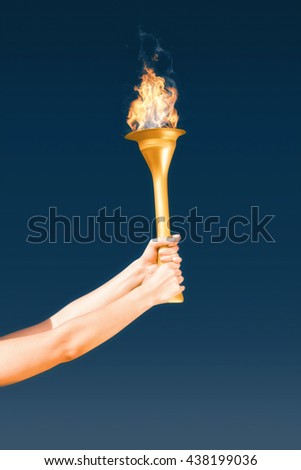 Sporty woman holding Olympic torch against navy sky