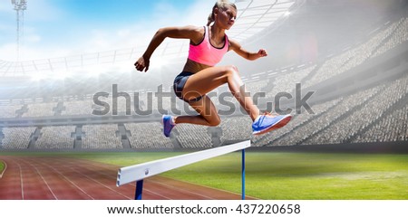 Sporty woman jumping a hurdle against view of a stadium