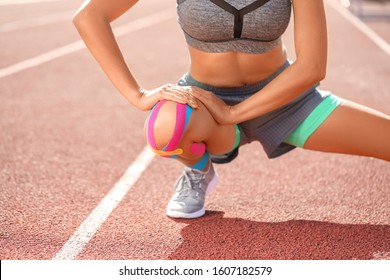 Sporty woman with physio tape stretching at stadium