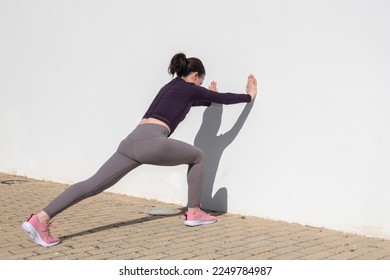 Sporty woman pushing against a white wall, warm up exercises. - Powered by Shutterstock