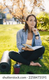 Sporty woman relaxing after workout by sitting and reading book in public garden on holiday. Happy lifestyle. Summer vacation. Workout sport concept. Green - Shutterstock ID 2258473191