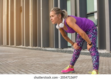 Sporty Woman Resting Has White Headphones.
40 Year Old Blonde Woman Resting While Doing Her Daily Exercise Routine In The City.