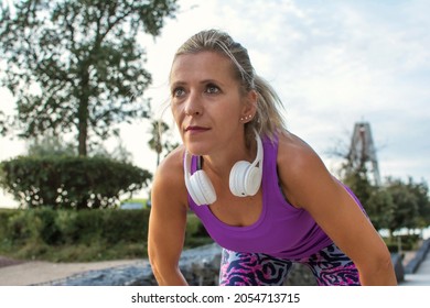 Sporty Woman Resting Has White Headphones.
40 Year Old Blonde Woman Resting While Doing Her Daily Exercise Routine In The City.